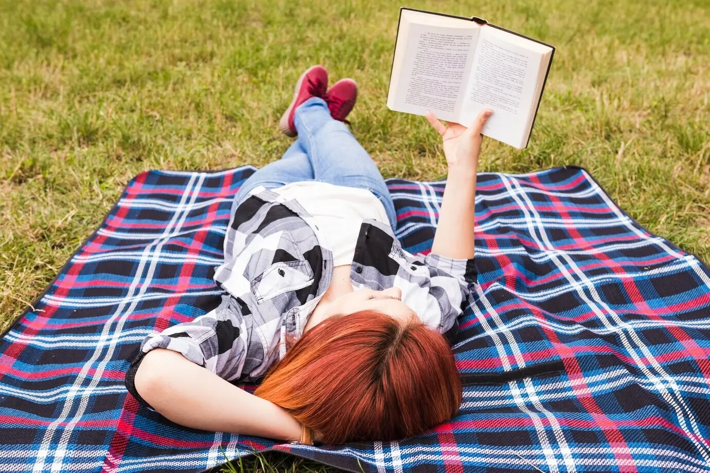 Eine junge Frau liegt auf einer Decke und liest ein Buch.